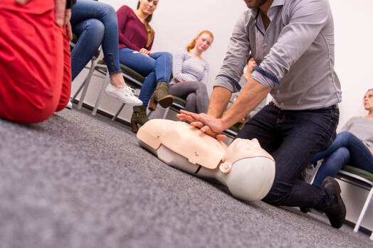 CPR first aid instructor applying rib cage compressions during in-class demonstration. 